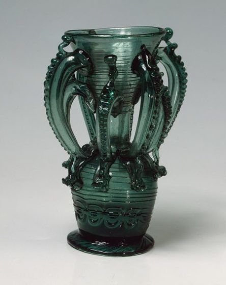 A tall, ornate green vase with eight handles