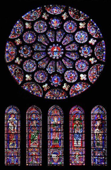 A circular stained glass window with five tall stained glass windows beneath it.