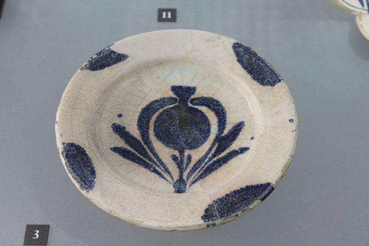 A blue and white dish featuring a rough painting of pomegranate plant in the center.