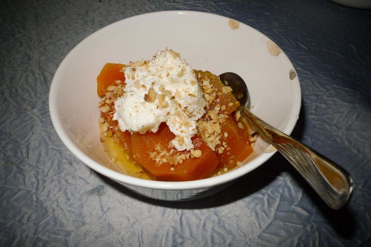 A pumpkin dessert in a bowl with kaymak and walnuts.