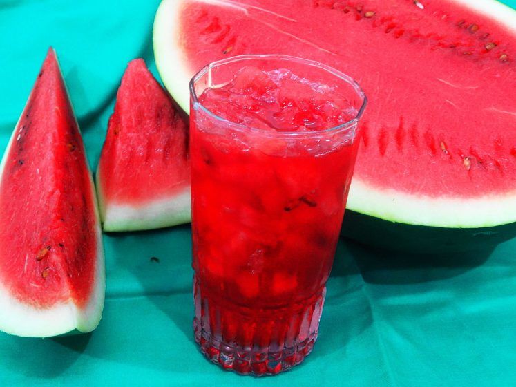 A glass of sharbat with watermelon in the background.