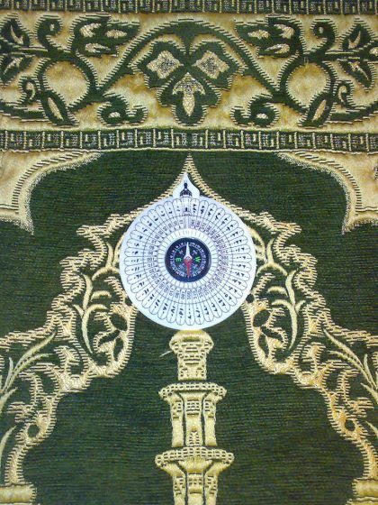 A white compass on a green and gold prayer rug.