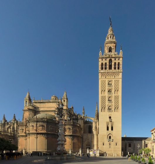 A large beige tower, the Giralda, next to a smaller building.