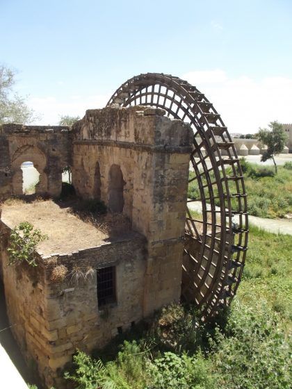 An ancient stone waterwheel on a small island in a river with a stone bridge in the background