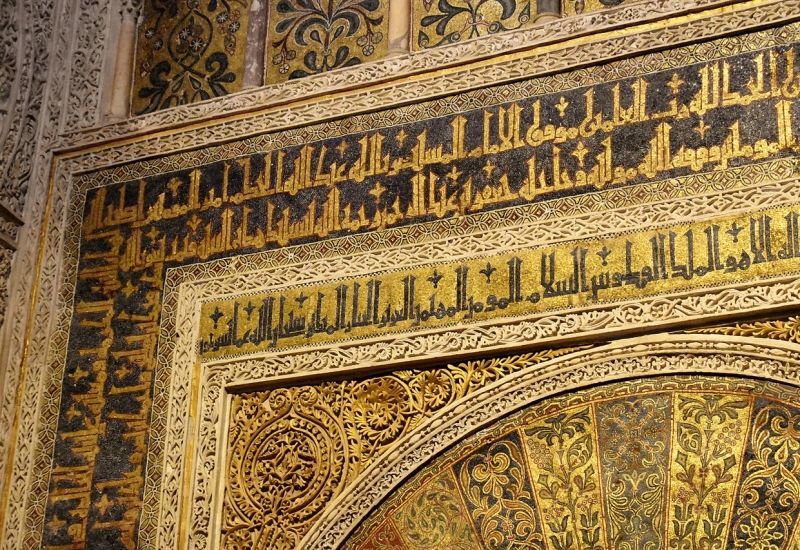 Ornate black and gold Arabic inscriptions on a corner of a wall.